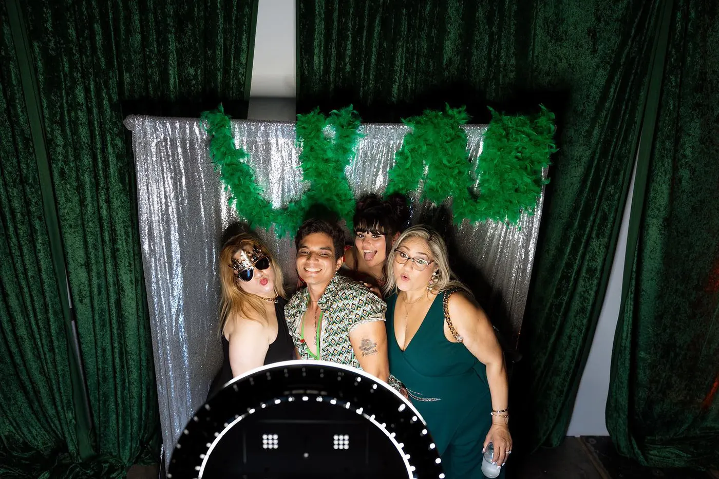 Party guests in novelty glasses in front of a greenery and sequin photo booth backdrop